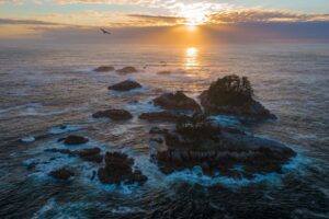 Orange sunset beams over crashing waves on rocky shore